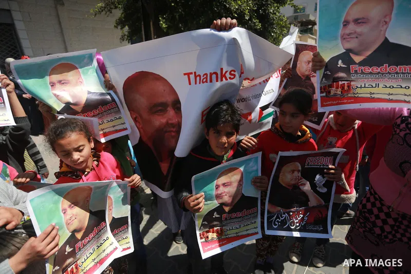 Palestinians hold posters of Mohammad El Halabi, World Vision's manager of operations in Gaza who was accused by Israel of funnelling millions of dollars in aid money to Hamas, during a protest in solidarity with El Hala...
