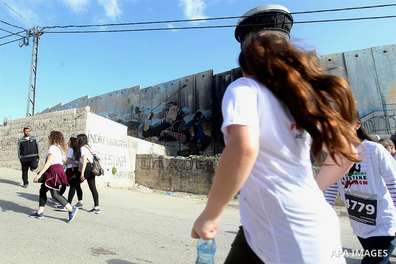 Participants run along Israel's controversial separation barrier, which divides the West Bank from Jerusalem, in the biblical West Bank town of Bethlehem during the 5th Palestine Marathon on March 31, 2017. Photo by Wisa...