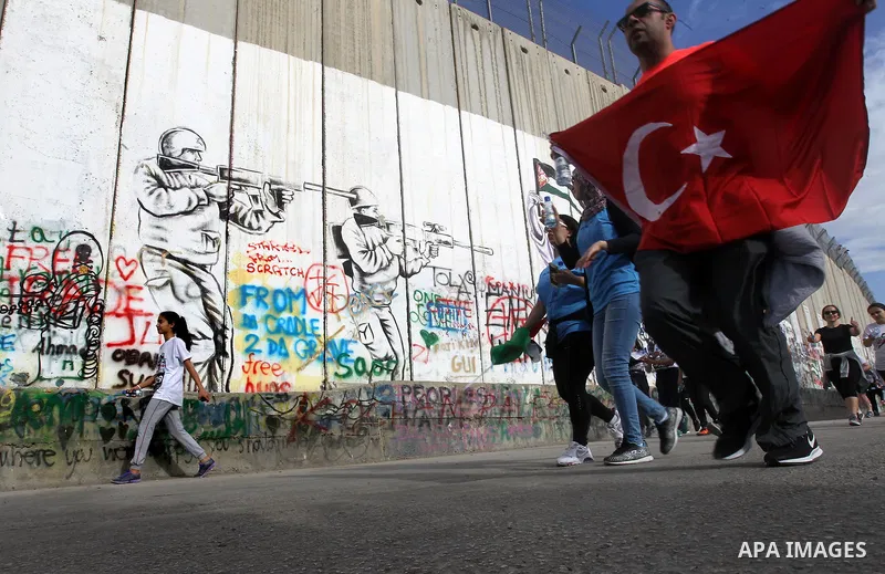 Participants run along Israel's controversial separation barrier, which divides the West Bank from Jerusalem, in the biblical West Bank town of Bethlehem during the 5th Palestine Marathon on March 31, 2017. Photo by Wisa...