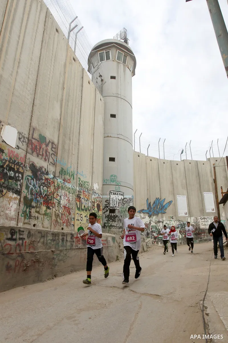 Participants run along Israel's controversial separation barrier, which divides the West Bank from Jerusalem, in the biblical West Bank town of Bethlehem during the 5th Palestine Marathon on March 31, 2017. Photo by Wisa...