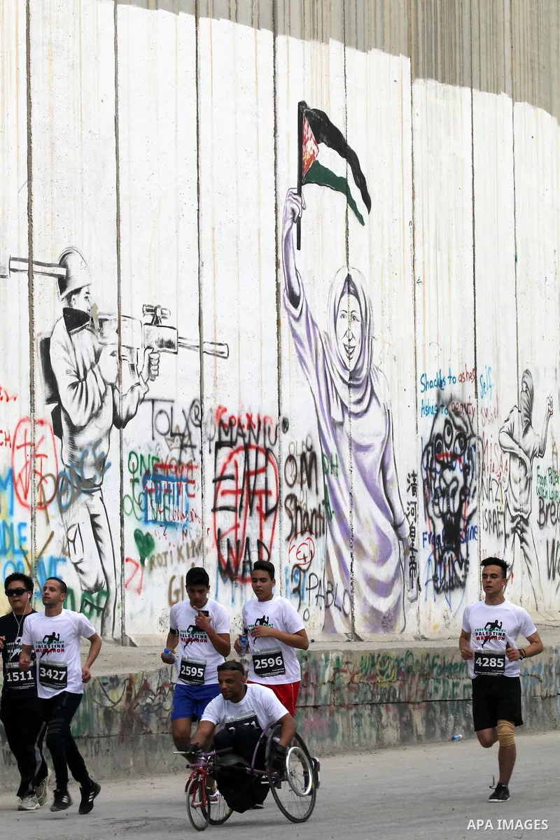 Participants run along Israel's controversial separation barrier, which divides the West Bank from Jerusalem, in the biblical West Bank town of Bethlehem during the 5th Palestine Marathon on March 31, 2017. Photo by Wisa...