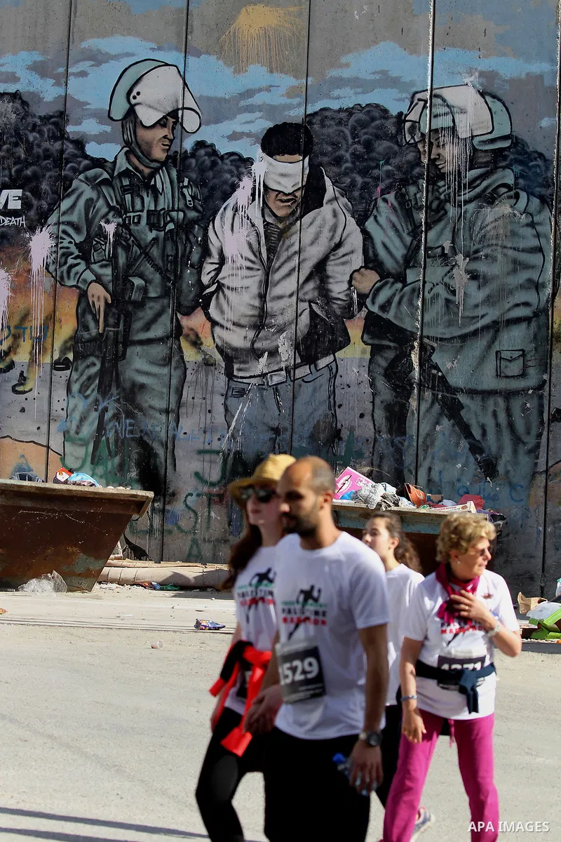 Participants run along Israel's controversial separation barrier, which divides the West Bank from Jerusalem, in the biblical West Bank town of Bethlehem during the 5th Palestine Marathon on March 31, 2017. Photo by Wisa...