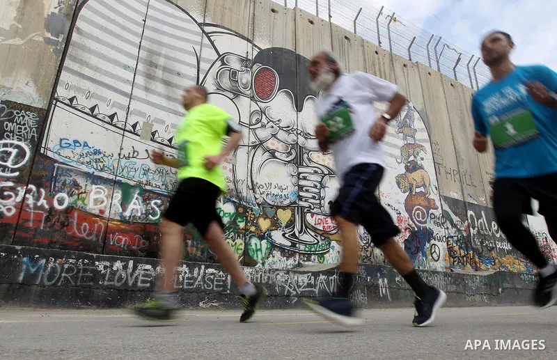 Participants run along Israel's controversial separation barrier, which divides the West Bank from Jerusalem, in the biblical West Bank town of Bethlehem during the 5th Palestine Marathon on March 31, 2017. Photo by Wisa...