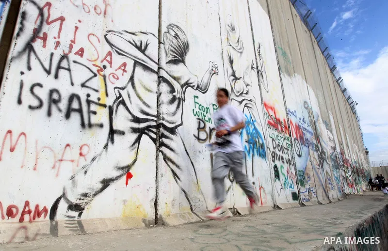 Participants run along Israel's controversial separation barrier, which divides the West Bank from Jerusalem, in the biblical West Bank town of Bethlehem during the 5th Palestine Marathon on March 31, 2017. Photo by Wisa...