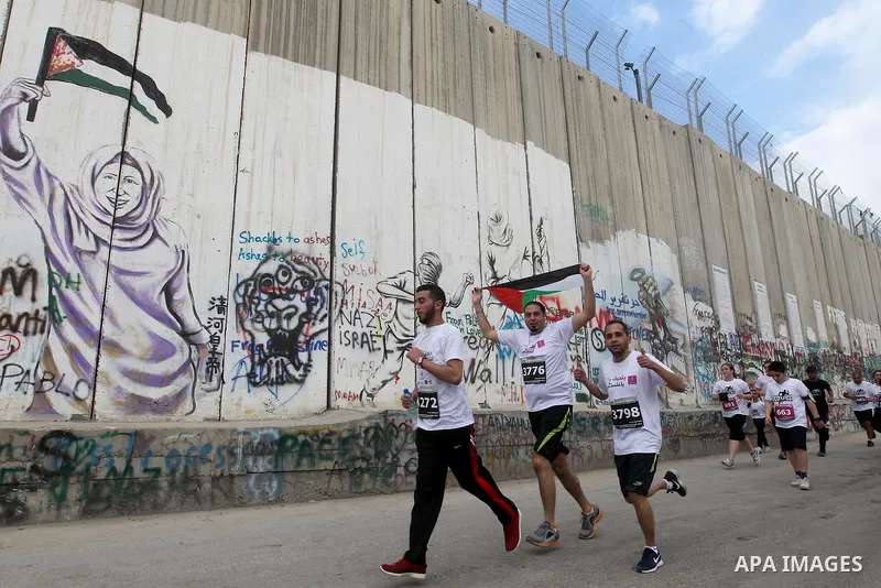 Participants run along Israel's controversial separation barrier, which divides the West Bank from Jerusalem, in the biblical West Bank town of Bethlehem during the 5th Palestine Marathon on March 31, 2017. Photo by Wisa...