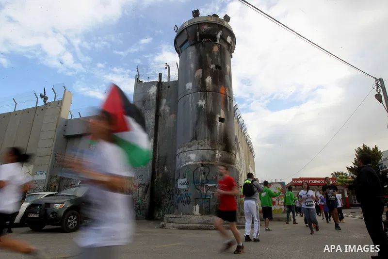 Participants run along Israel's controversial separation barrier, which divides the West Bank from Jerusalem, in the biblical West Bank town of Bethlehem during the 5th Palestine Marathon on March 31, 2017. Photo by Wisa...