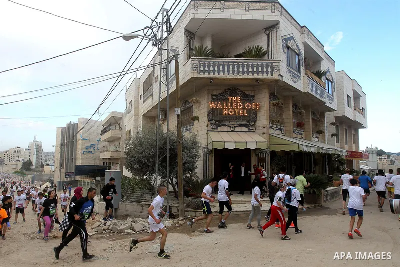 Participants run past the the Walled-Off Hotel, Banksy's newly opened hotel, next to Israel's controversial separation wall, during the fifth Palestine Marathon in the biblical West Bank town of Bethlehem, on March 31, 2...