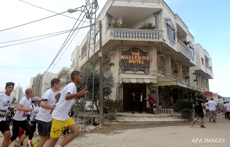 Participants run past the the Walled-Off Hotel, Banksy's newly opened hotel, next to Israel's controversial separation wall, during the fifth Palestine Marathon in the biblical West Bank town of Bethlehem, on March 31, 2...