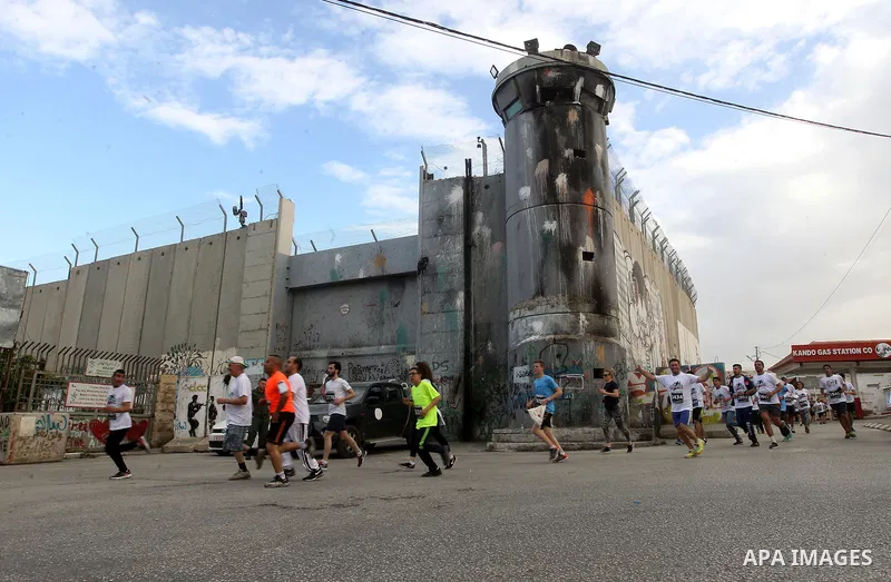 Participants run along Israel's controversial separation barrier, which divides the West Bank from Jerusalem, in the biblical West Bank town of Bethlehem during the 5th Palestine Marathon on March 31, 2017. Photo by Wisa...