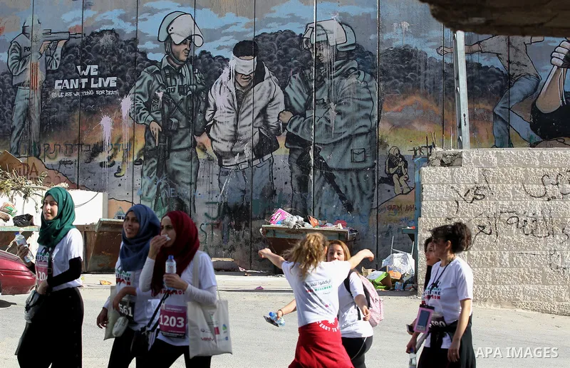 Participants run along Israel's controversial separation barrier, which divides the West Bank from Jerusalem, in the biblical West Bank town of Bethlehem during the 5th Palestine Marathon on March 31, 2017. Photo by Wisa...