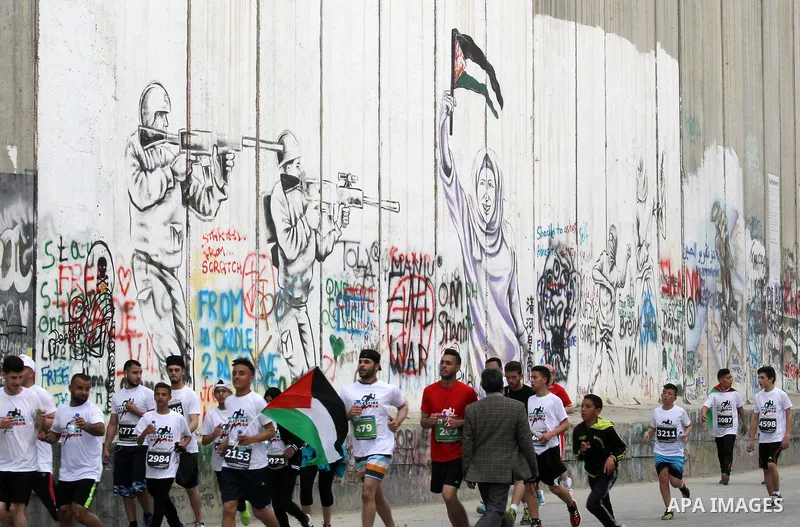 Participants run along Israel's controversial separation barrier, which divides the West Bank from Jerusalem, in the biblical West Bank town of Bethlehem during the 5th Palestine Marathon on March 31, 2017. Photo by Wisa...