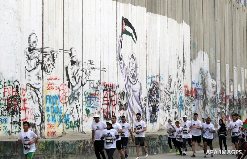 Participants run along Israel's controversial separation barrier, which divides the West Bank from Jerusalem, in the biblical West Bank town of Bethlehem during the 5th Palestine Marathon on March 31, 2017. Photo by Wisa...