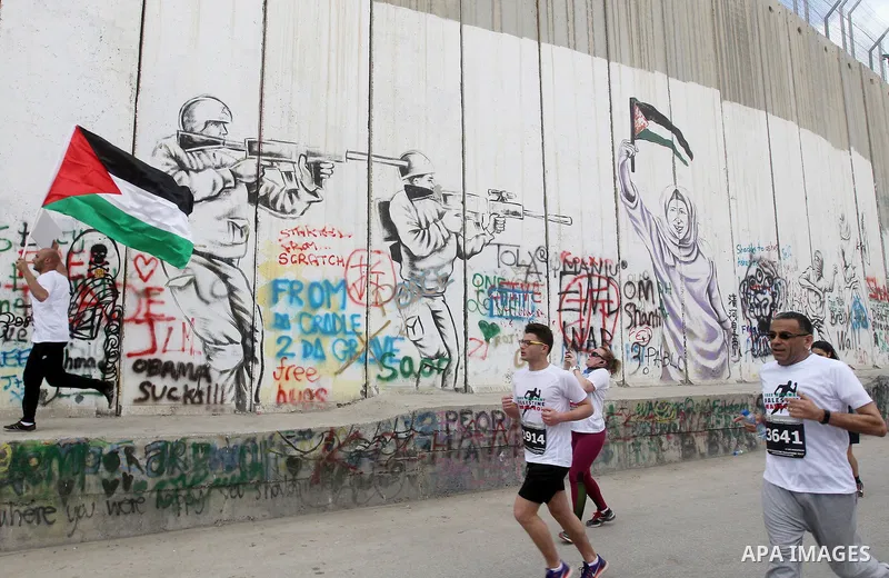 Participants run along Israel's controversial separation barrier, which divides the West Bank from Jerusalem, in the biblical West Bank town of Bethlehem during the 5th Palestine Marathon on March 31, 2017. Photo by Wisa...