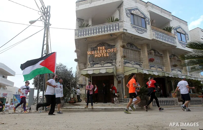 Participants run past the the Walled-Off Hotel, Banksy's newly opened hotel, next to Israel's controversial separation wall, during the fifth Palestine Marathon in the biblical West Bank town of Bethlehem, on March 31, 2...