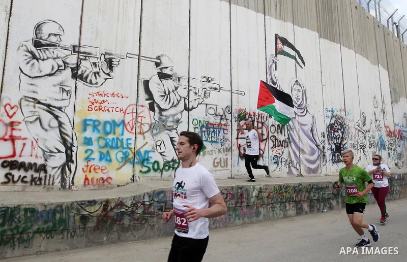 Participants run along Israel's controversial separation barrier, which divides the West Bank from Jerusalem, in the biblical West Bank town of Bethlehem during the 5th Palestine Marathon on March 31, 2017. Photo by Wisa...