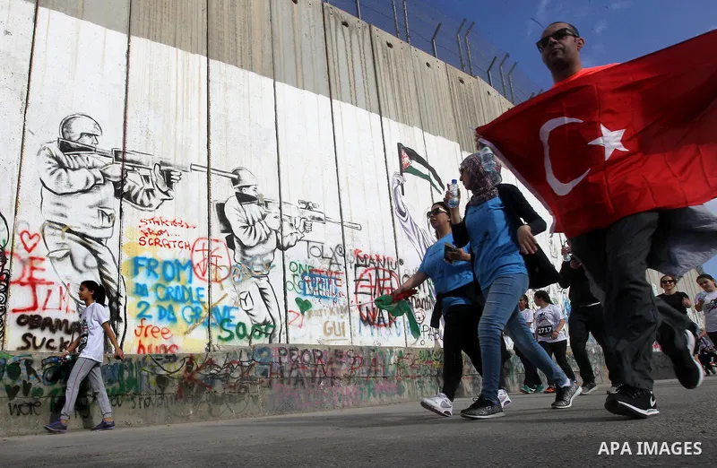 Participants run along Israel's controversial separation barrier, which divides the West Bank from Jerusalem, in the biblical West Bank town of Bethlehem during the 5th Palestine Marathon on March 31, 2017. Photo by Wisa...