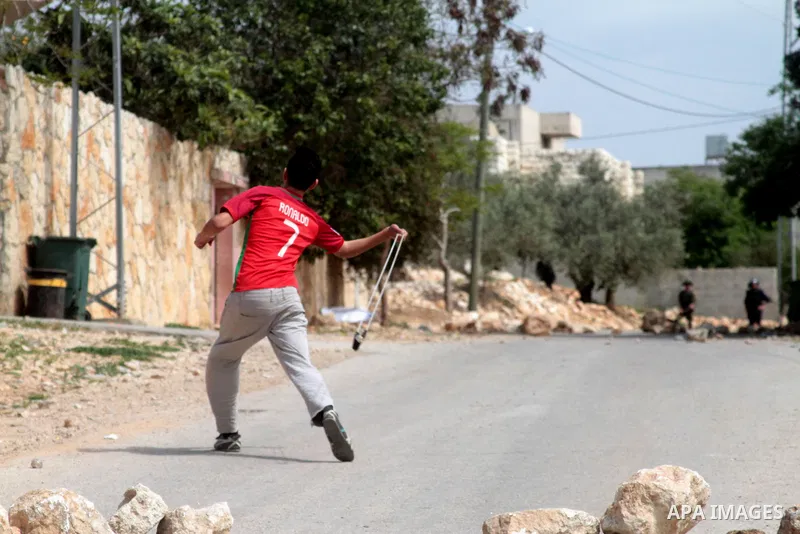 A Palestinian protester uses a slingshot to hurl stones towards Israeli security forces during clashes following a weekly demonstration against the expropriation of Palestinian land by Israel in the village of Kfar Qaddu...