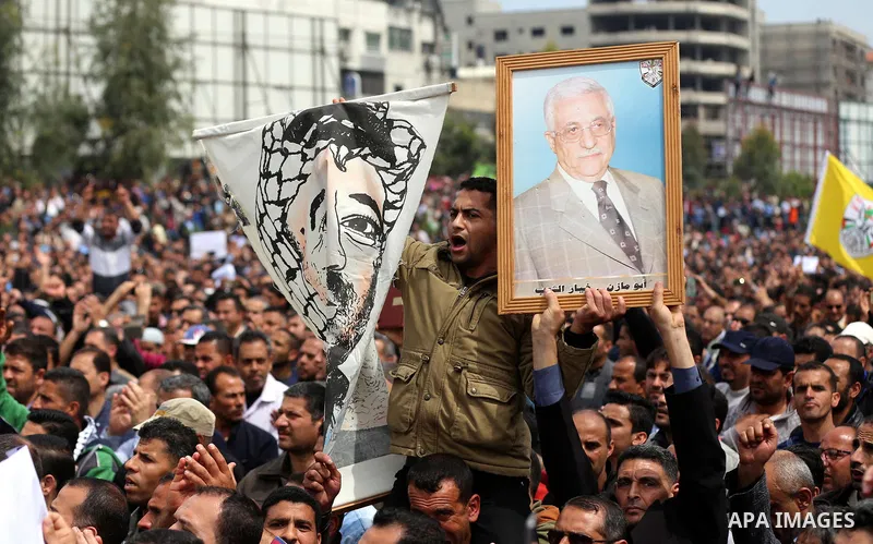A Palestinian Authority employee holds a painted poster depicting late Palestinian leader Yasser Arafat and a poster of President Mahmoud Abbas during a demonstration against the decision to reduce their salaries in Gaza...