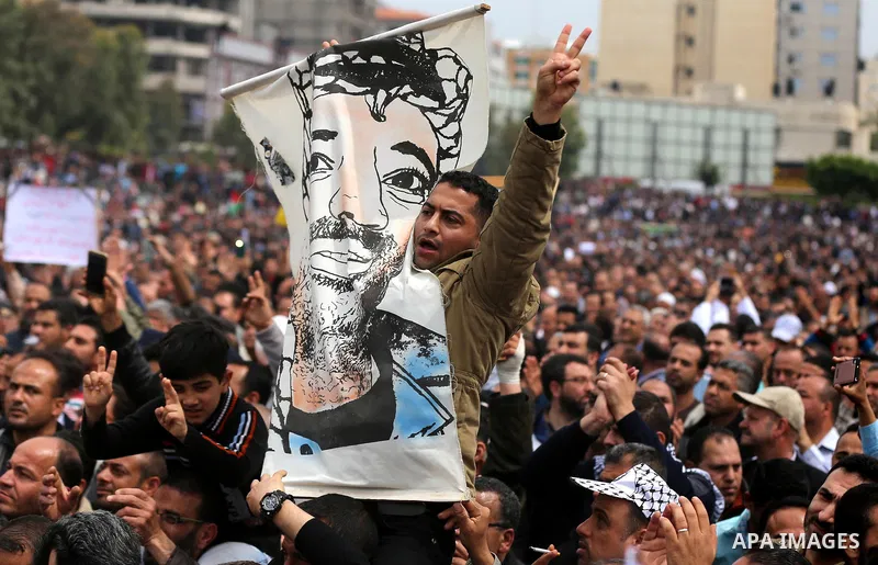 A Palestinian Authority employee holds a painted poster depicting late Palestinian leader Yasser Arafat during a demonstration against the decision to reduce their salaries in Gaza City on April 8, 2017. Photo by Ashraf...