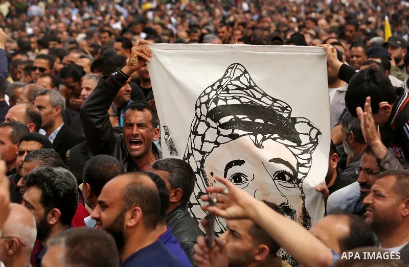 A Palestinian Authority employee holds a painted poster depicting late Palestinian leader Yasser Arafat during a demonstration against the decision to reduce their salaries in Gaza City on April 8, 2017. Photo by Ashraf...