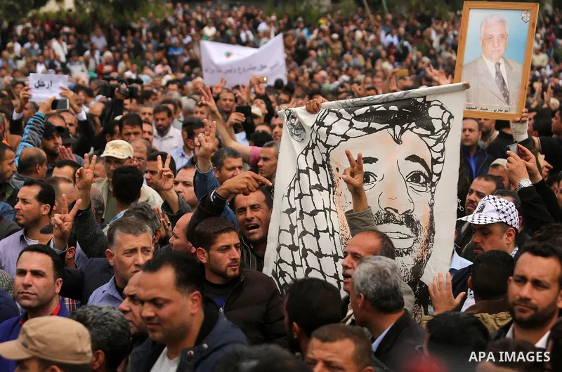 A Palestinian Authority employee holds a painted poster depicting late Palestinian leader Yasser Arafat and a poster of President Mahmoud Abbas during a demonstration against the decision to reduce their salaries in Gaza...