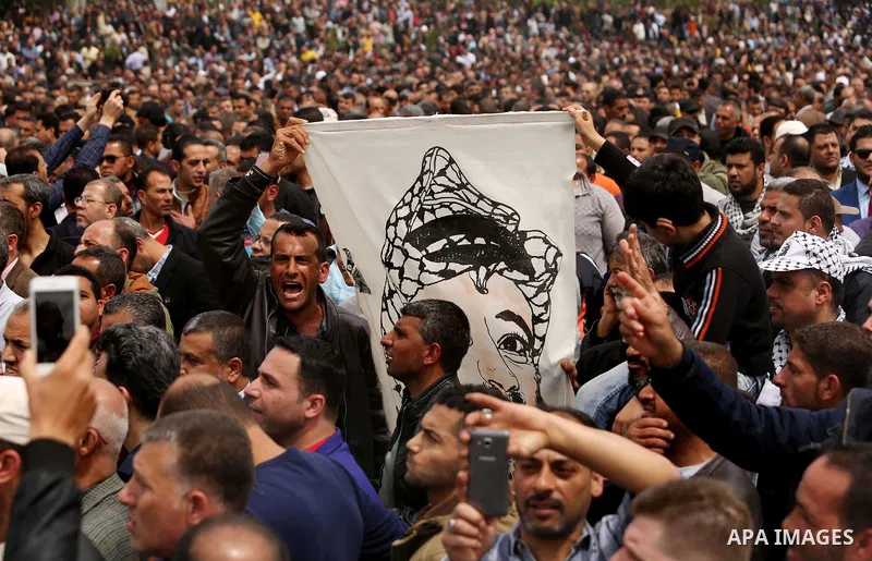 A Palestinian Authority employee holds a painted poster depicting late Palestinian leader Yasser Arafat during a demonstration against the decision to reduce their salaries in Gaza City on April 8, 2017. Photo by Ashraf...