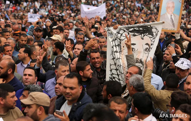 A Palestinian Authority employee holds a painted poster depicting late Palestinian leader Yasser Arafat and a poster of President Mahmoud Abbas during a demonstration against the decision to reduce their salaries in Gaza...