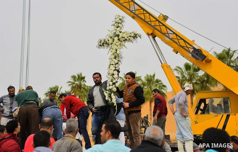 Egyptian workers use crane to lift coffins of the victims of the blast at the Coptic Christian Saint Mark's church in Alexandria the previous day during a funeral procession at the Monastery of Marmina in the city of Bor...