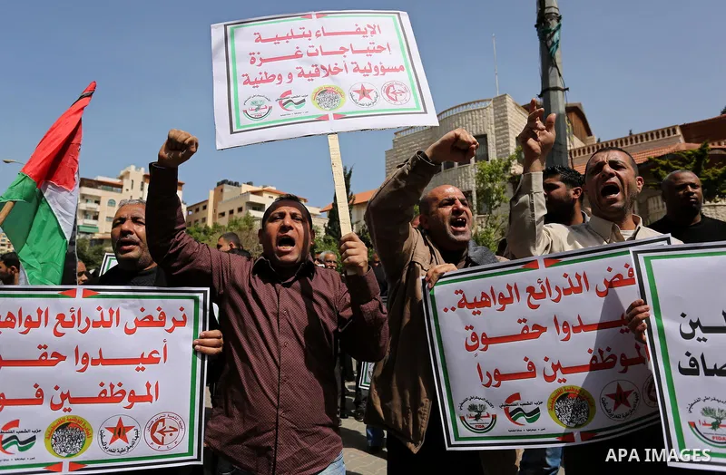Palestinians employed by the Palestinian Authority, chant slogans and wave placards during a demonstration against the decision to reduce their salaries in Gaza City on April 11, 2017. Photo by Ashraf Amra