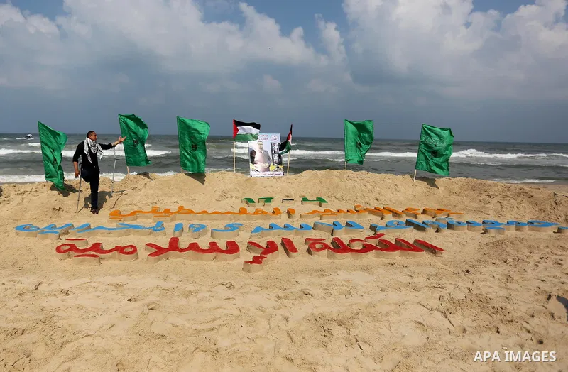 Palestinians stand next to an art installation by a Palestinian artist Mohammed Totah which he outlines in sand to mark the Palestinian Prisoner day, on Gaza City's Mediterranean shore on April 15, 2017. Photo by Ashraf...