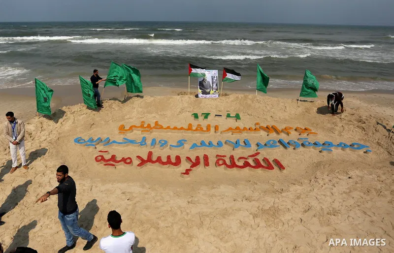 Palestinians stand next to an art installation by a Palestinian artist Mohammed Totah which he outlines in sand to mark the Palestinian Prisoner day, on Gaza City's Mediterranean shore on April 15, 2017. Photo by Ashraf...