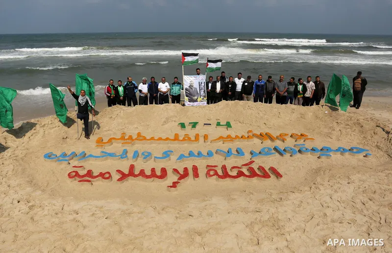 Palestinians stand next to an art installation by a Palestinian artist Mohammed Totah which he outlines in sand to mark the Palestinian Prisoner day, on Gaza City's Mediterranean shore on April 15, 2017. Photo by Ashraf...