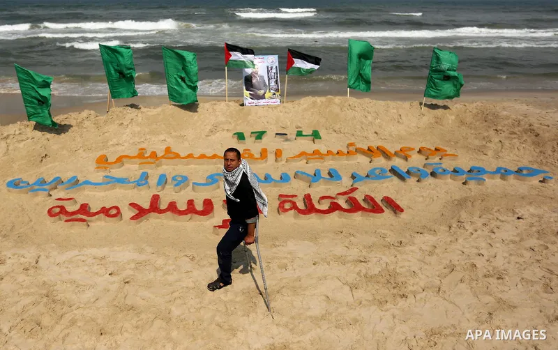 A Palestinian artist Mohammed Totah stand next to his art installation which he outlines in sand to mark the Palestinian Prisoner day, on Gaza City's Mediterranean shore on April 15, 2017. Photo by Ashraf Amra