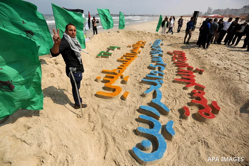 Palestinians stand next to an art installation by a Palestinian artist Mohammed Totah which he outlines in sand to mark the Palestinian Prisoner day, on Gaza City's Mediterranean shore on April 15, 2017. Photo by Ashraf...