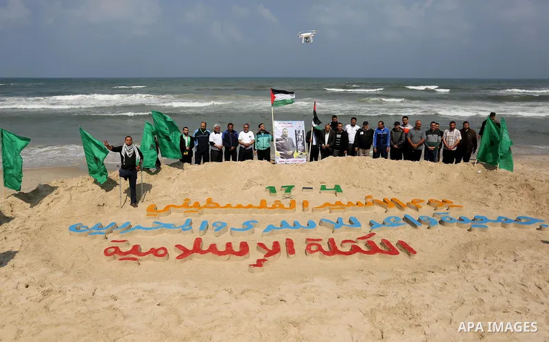 Palestinians stand next to an art installation by a Palestinian artist Mohammed Totah which he outlines in sand to mark the Palestinian Prisoner day, on Gaza City's Mediterranean shore on April 15, 2017. Photo by Ashraf...