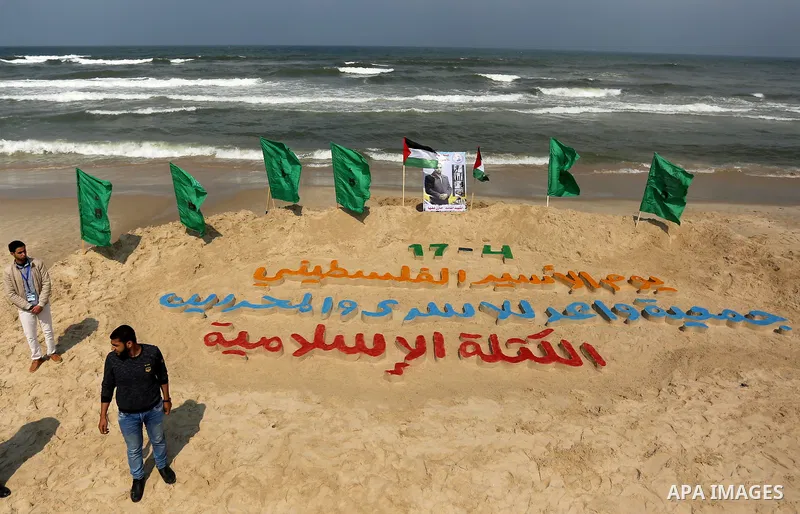 Palestinians stand next to an art installation by a Palestinian artist Mohammed Totah which he outlines in sand to mark the Palestinian Prisoner day, on Gaza City's Mediterranean shore on April 15, 2017. Photo by Ashraf...