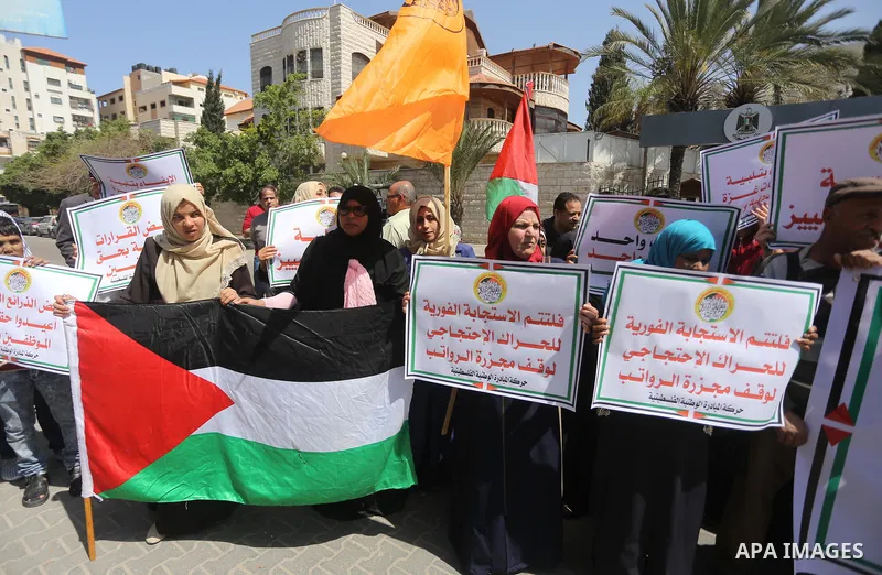 Palestinians hold placards during a demonstration against the decision to reduce their salaries in Gaza City on April 18, 2017. Photo by Mohammed Asad