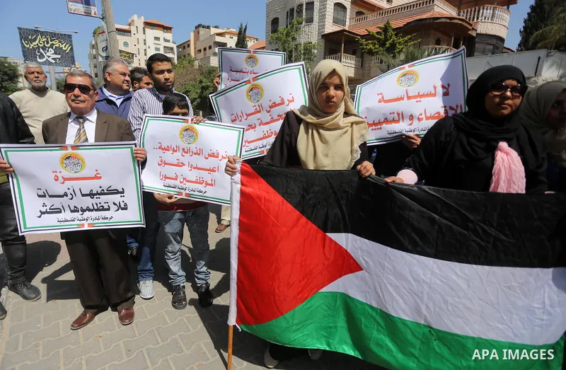 Palestinians hold placards during a demonstration against the decision to reduce their salaries in Gaza City on April 18, 2017. Photo by Mohammed Asad