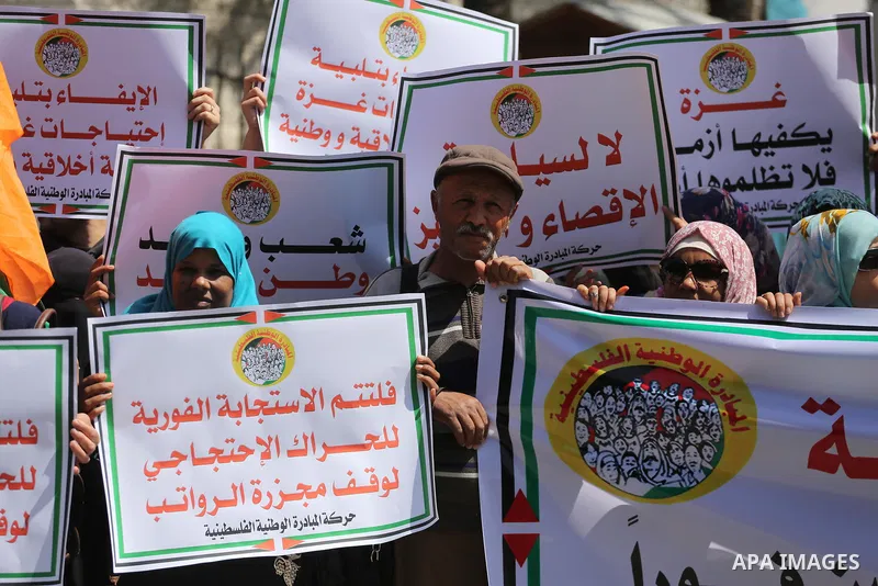 Palestinians hold placards during a demonstration against the decision to reduce their salaries in Gaza City on April 18, 2017. Photo by Mohammed Asad