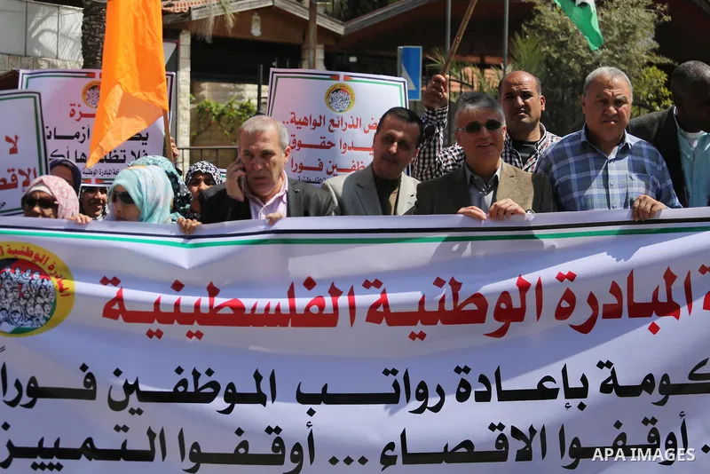 Palestinians hold placards during a demonstration against the decision to reduce their salaries in Gaza City on April 18, 2017. Photo by Mohammed Asad