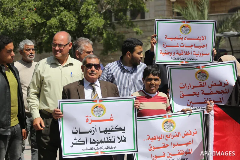 Palestinians hold placards during a demonstration against the decision to reduce their salaries in Gaza City on April 18, 2017. Photo by Mohammed Asad