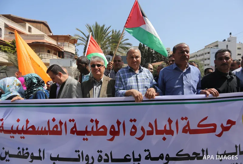 Palestinians hold placards during a demonstration against the decision to reduce their salaries in Gaza City on April 18, 2017. Photo by Mohammed Asad