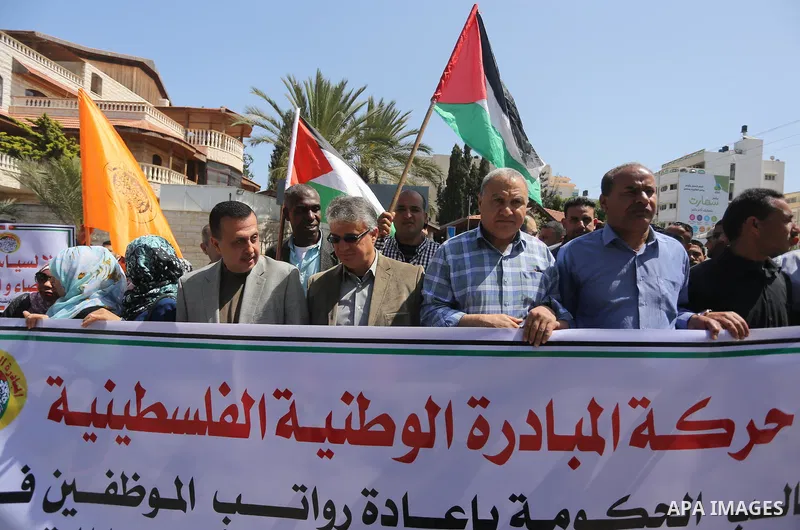 Palestinians hold placards during a demonstration against the decision to reduce their salaries in Gaza City on April 18, 2017. Photo by Mohammed Asad