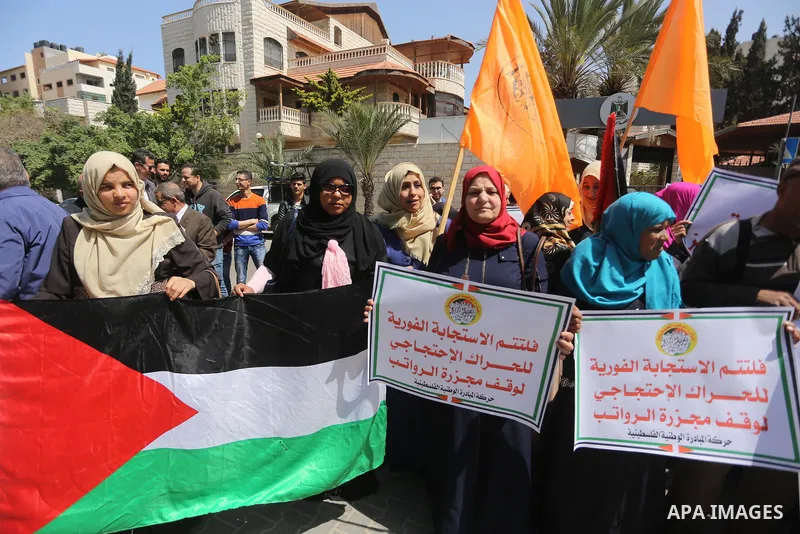 Palestinians hold placards during a demonstration against the decision to reduce their salaries in Gaza City on April 18, 2017. Photo by Mohammed Asad