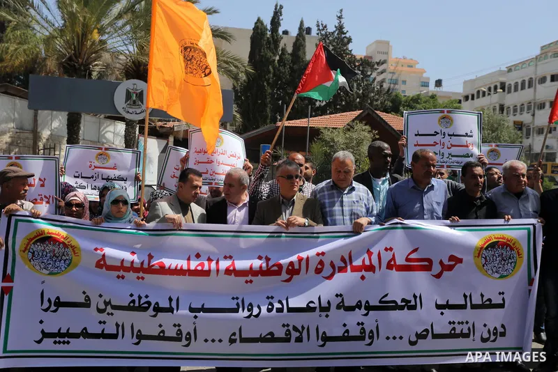 Palestinians hold placards during a demonstration against the decision to reduce their salaries in Gaza City on April 18, 2017. Photo by Mohammed Asad