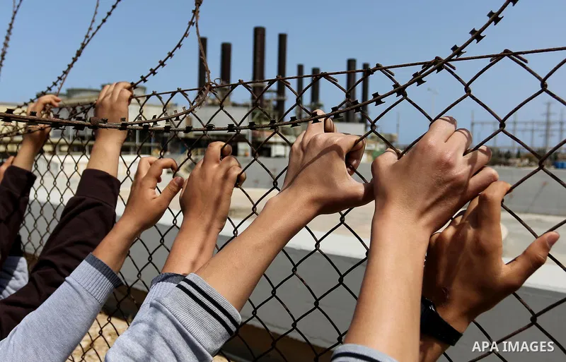 Palestinian school boys stand by a fence during a protest calling for an end to the power crisis, outside the power plant in the central Gaza Strip April 23, 2017. Photo by Ashraf Amra