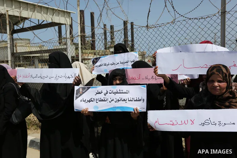 Palestinian women hold banners during a protest calling for an end to the power crisis, outside the power plant in the central Gaza Strip April 23, 2017. Photo by Ashraf Amra