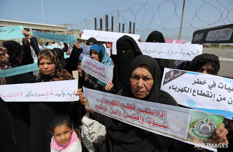 Palestinian women hold banners during a protest calling for an end to the power crisis, outside the power plant in the central Gaza Strip April 23, 2017. Photo by Ashraf Amra