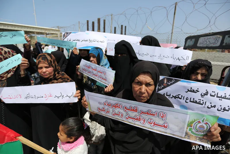 Palestinian women hold banners during a protest calling for an end to the power crisis, outside the power plant in the central Gaza Strip April 23, 2017. Photo by Ashraf Amra