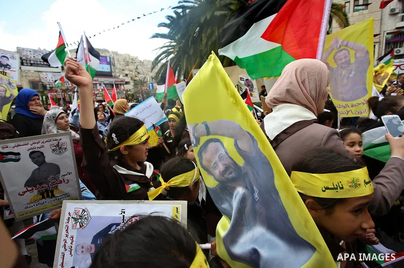 Palestinian protesters wave flags bearing the portrait of prominent prisoner and popular leader Marwan Barghouti during a demonstration in solidarity with Palestinian prisoners on hunger strike in Israeli jails, in the W...